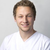 Nahaufnahme eines lächelnden Mannes mit braunem Haar und Bart im weißen T-Shirt vor hellem Hintergrund