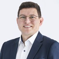 Lächelnder Mann mit Brille im dunkelblauen Anzug und weißem Hemd vor hellem Hintergrund
